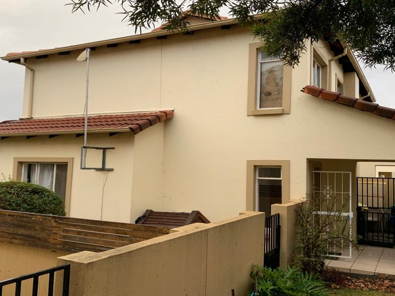 Rear view of a two-story apartment building featuring plastered walls, a tiled roof, and a secure gated entrance.
