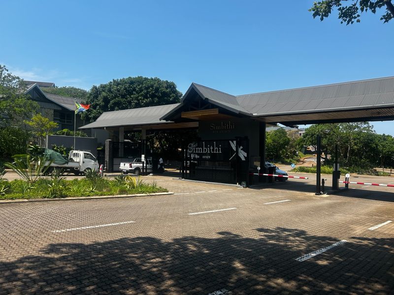 The main entrance gate and security checkpoint for Simbithi Eco Estate, featuring a paved driveway, boom gates, and modern architectural signage.