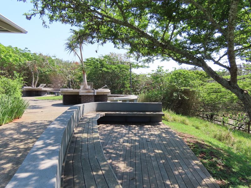 Outdoor entertainment area featuring built-in concrete seating, timber decking, and a brick braai facility set within a landscaped garden environment.