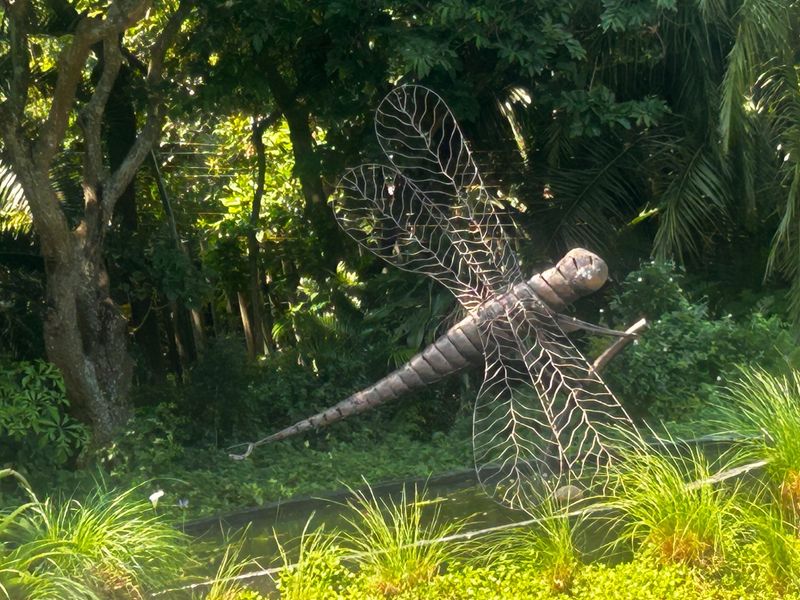 A lush, landscaped garden area featuring mature trees, ornamental grasses, and a decorative water feature with a dragonfly sculpture.