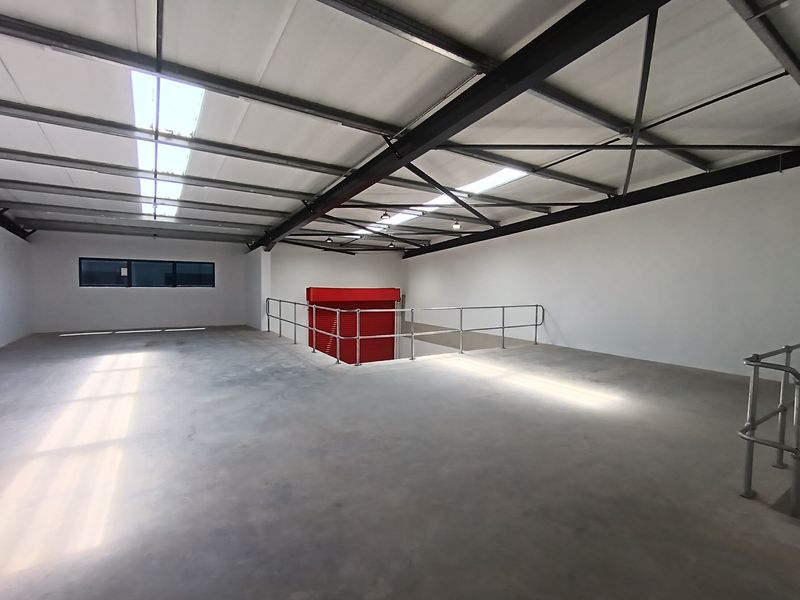 Spacious industrial mezzanine level featuring concrete flooring, steel safety railings, and natural light provided by integrated roof skylights.