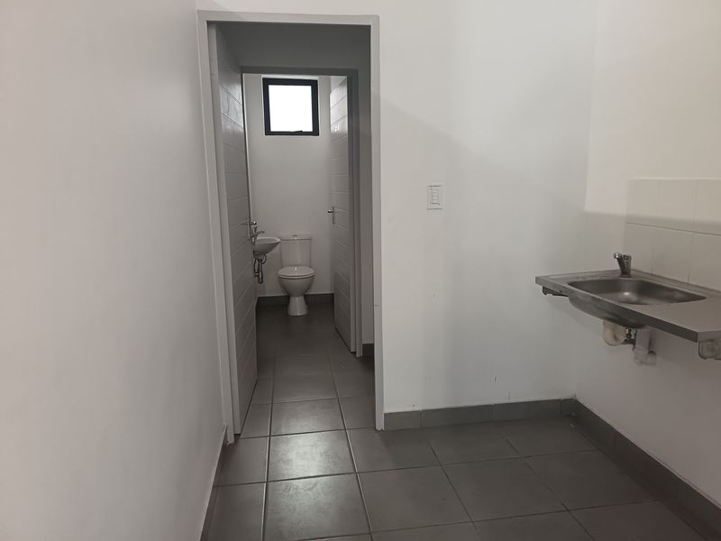 A functional utility area featuring a stainless steel sink and an adjoining small bathroom with a toilet and basin, finished with neutral floor tiles.