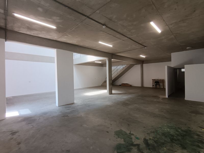 Spacious open-plan industrial unit featuring exposed concrete ceilings, polished concrete flooring, and a central staircase, offering a versatile blank canvas for various business operations.