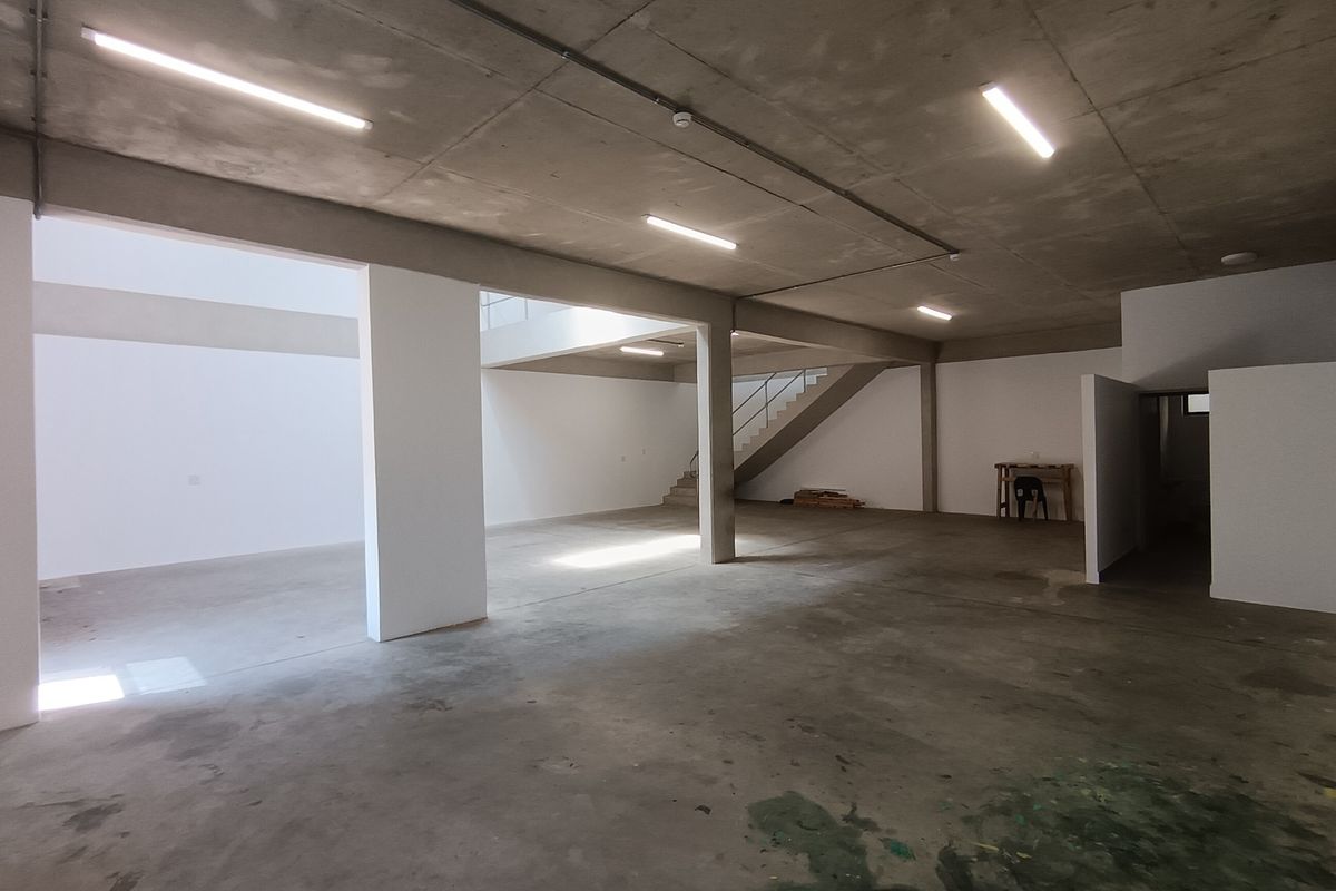 Spacious open-plan industrial unit featuring exposed concrete ceilings, polished concrete flooring, and a central staircase, offering a versatile blank canvas for various business operations.