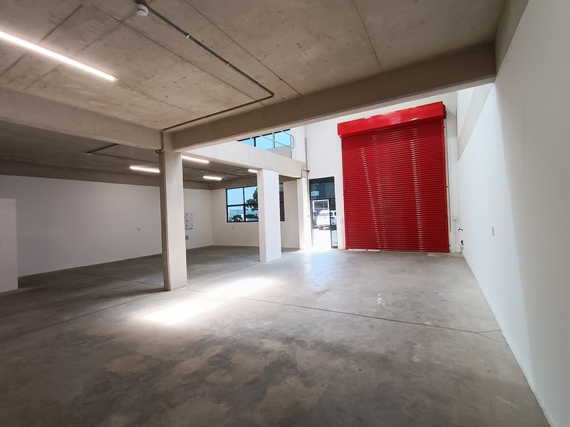 Spacious industrial utility area featuring polished concrete floors, exposed concrete ceilings, and a large red roller shutter door for easy access.