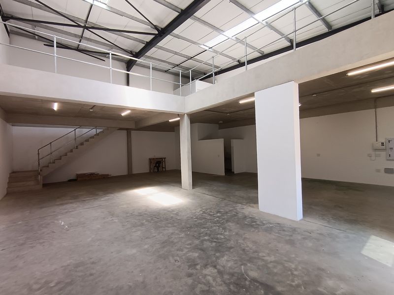 Spacious industrial unit featuring a mezzanine level, concrete flooring, exposed steel roof trusses, and natural light from overhead skylights.