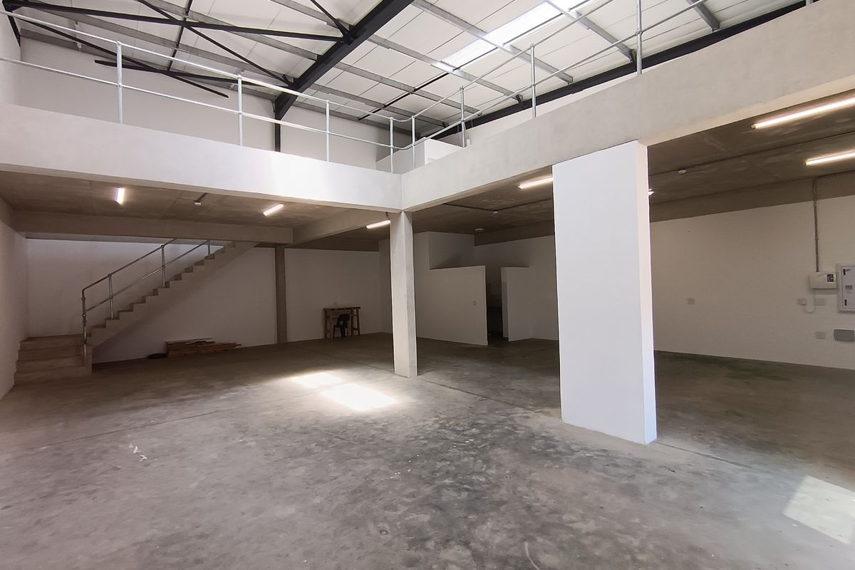 Spacious industrial unit featuring a mezzanine level, concrete flooring, exposed steel roof trusses, and natural light from overhead skylights.