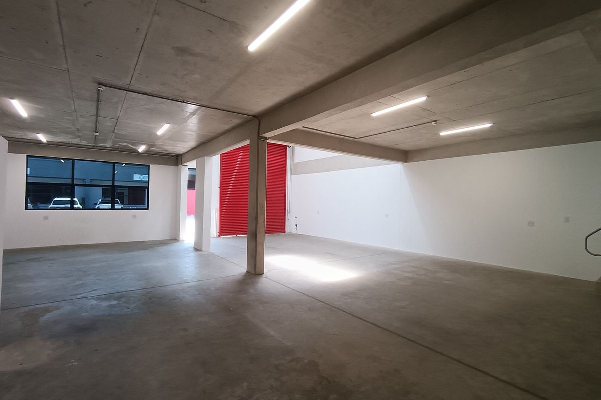 Spacious industrial utility area featuring concrete flooring, exposed concrete ceilings, bright fluorescent lighting, and a large red roller shutter door.
