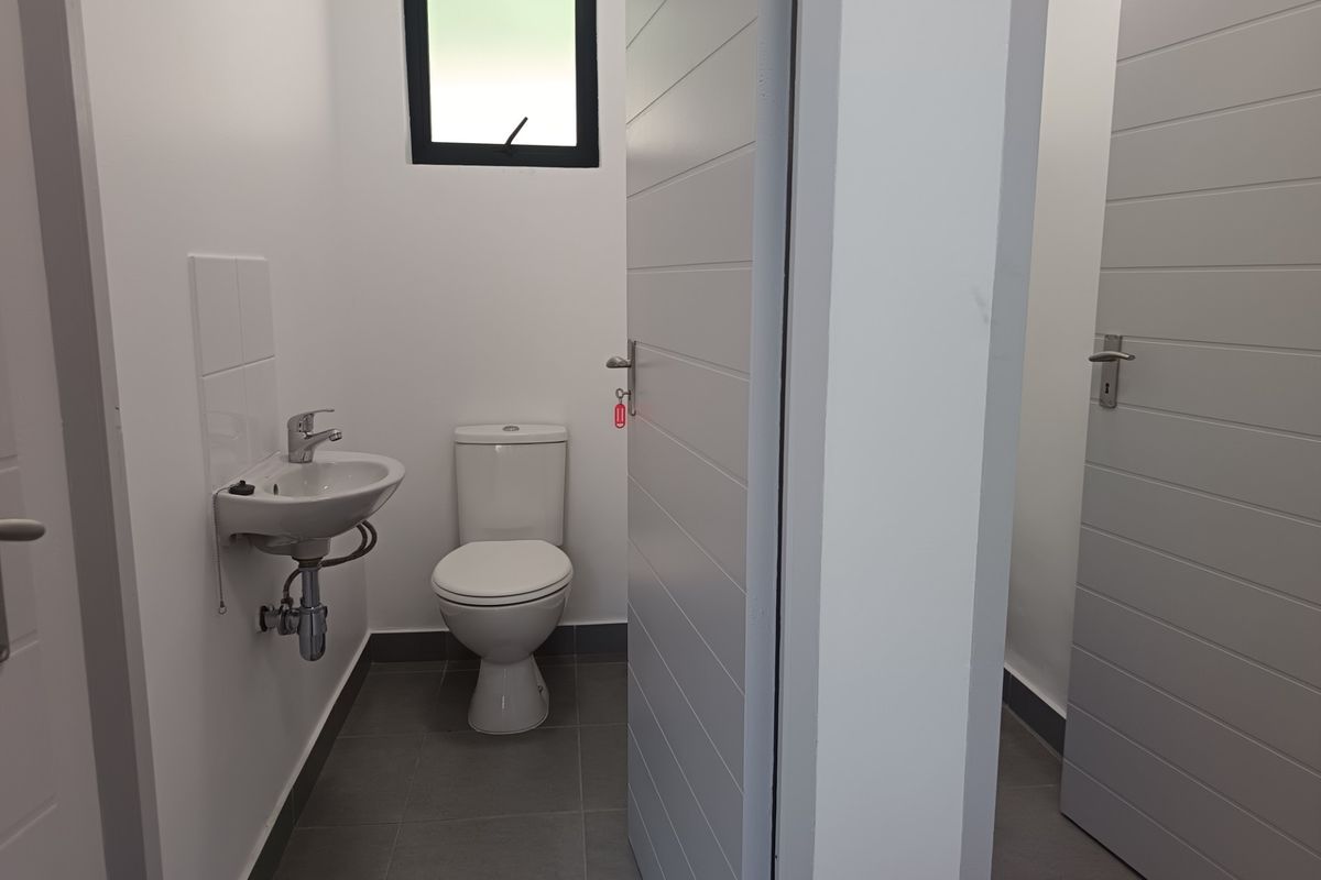 A clean, modern bathroom featuring a wall-mounted basin, toilet, tiled flooring, and neutral finishes, presenting in excellent condition.