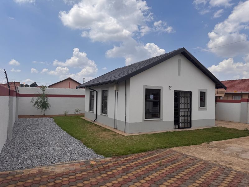 A well-maintained detached house featuring a tiled roof, paved driveway, and secure perimeter wall with electric fencing in a neat garden setting.