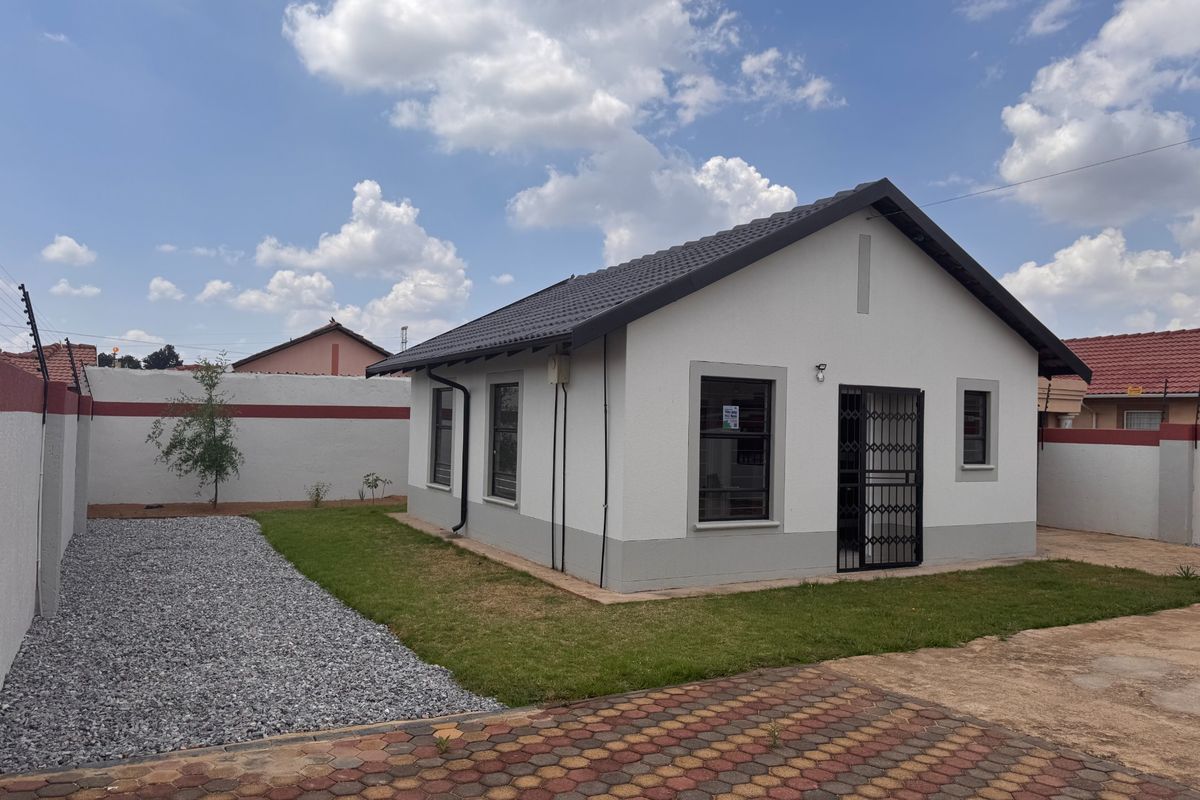 A well-maintained detached house featuring a tiled roof, paved driveway, and secure perimeter wall with electric fencing in a neat garden setting.