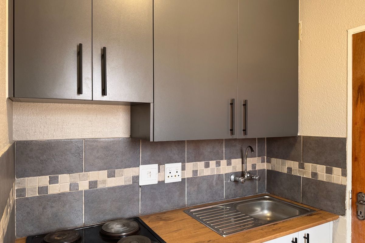 Compact kitchen area featuring modern grey cabinetry, a wooden countertop, integrated electric hob, and a stainless steel sink with tiled backsplash.