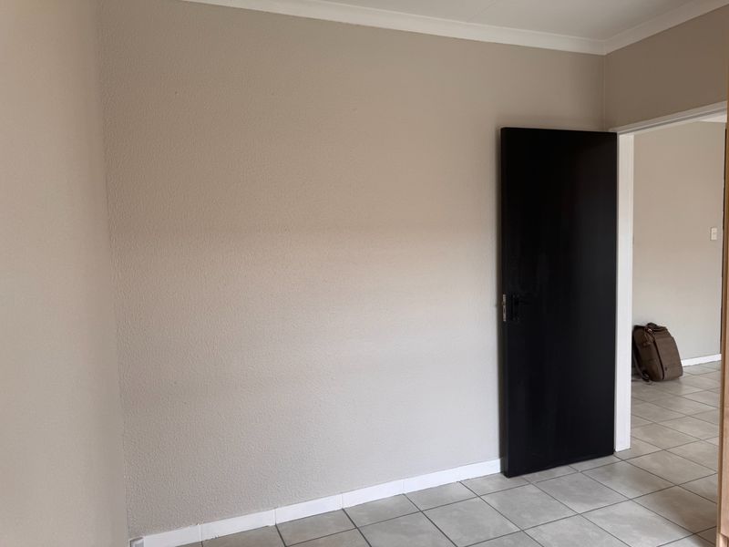 A clean, empty bedroom featuring neutral painted walls, tiled flooring, and a dark internal door, offering a blank canvas for personalization.