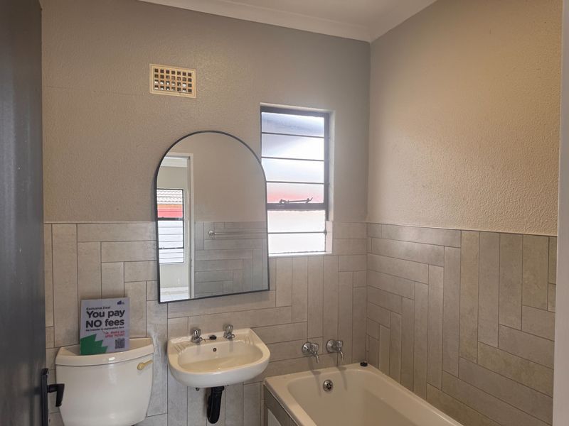 A clean, functional bathroom featuring a wall-mounted basin, bathtub, and modern herringbone-patterned wall tiling.