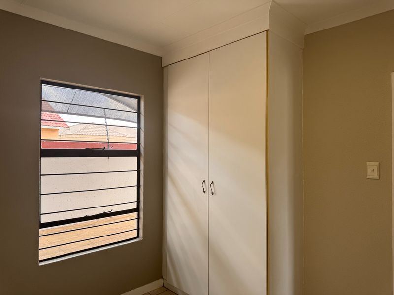 A clean bedroom featuring a built-in wardrobe and a window fitted with security bars, offering a neutral and functional space.
