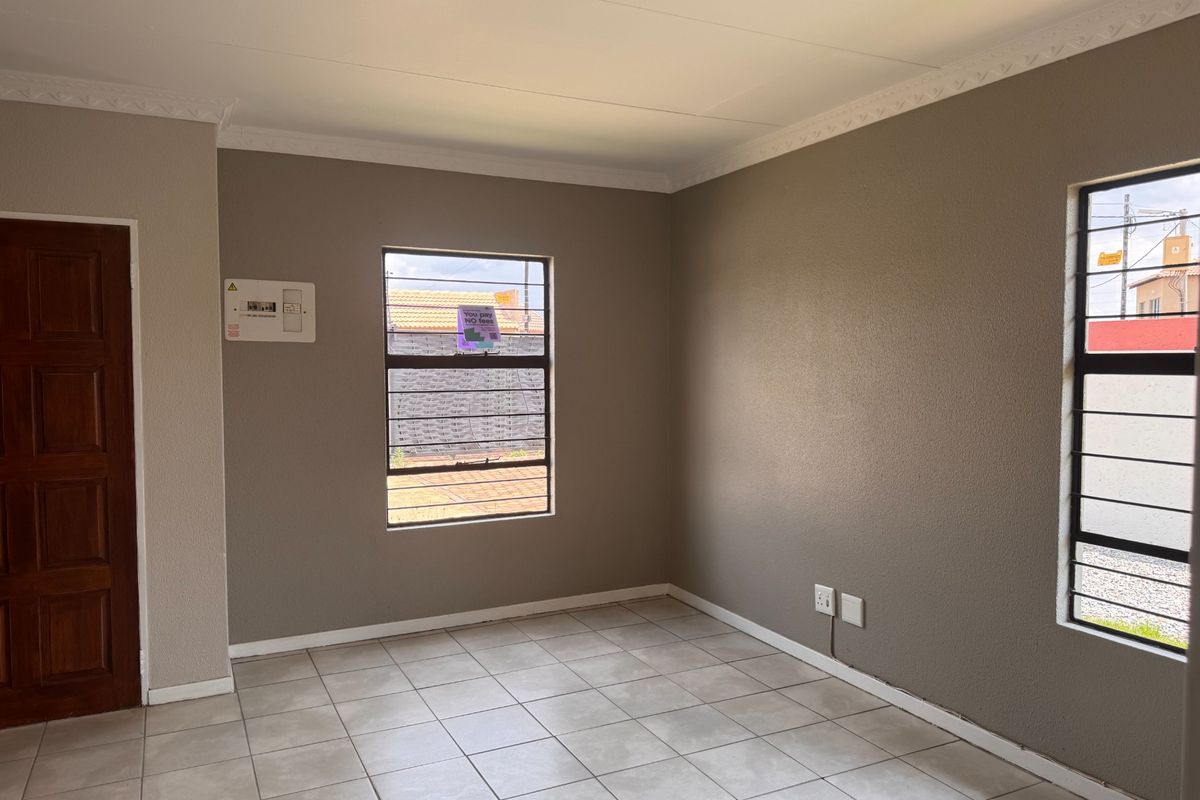 A bright, empty living area featuring neutral wall tones, tiled flooring, and secure window bars, providing a clean canvas for personalization.