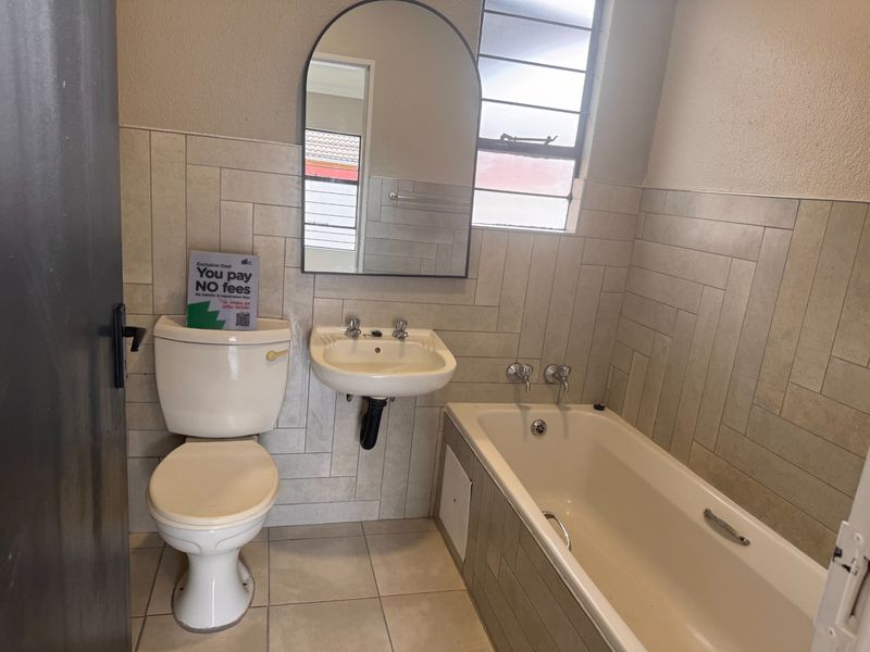 A functional bathroom featuring a wall-mounted basin, bathtub, and tiled finishes, offering a clean canvas for potential cosmetic updates.