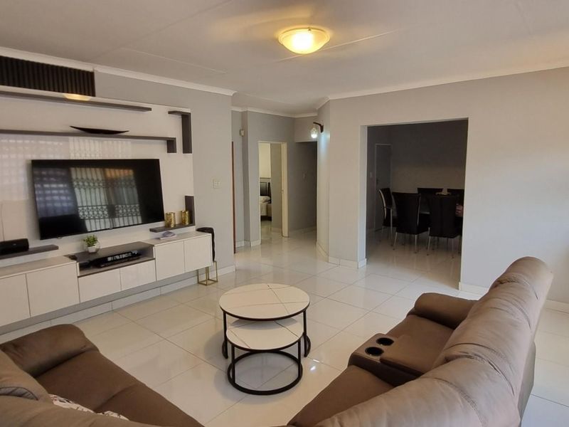 A well-maintained living room featuring modern tiled flooring, a sleek built-in media wall unit, and an open-plan layout leading to the dining area.