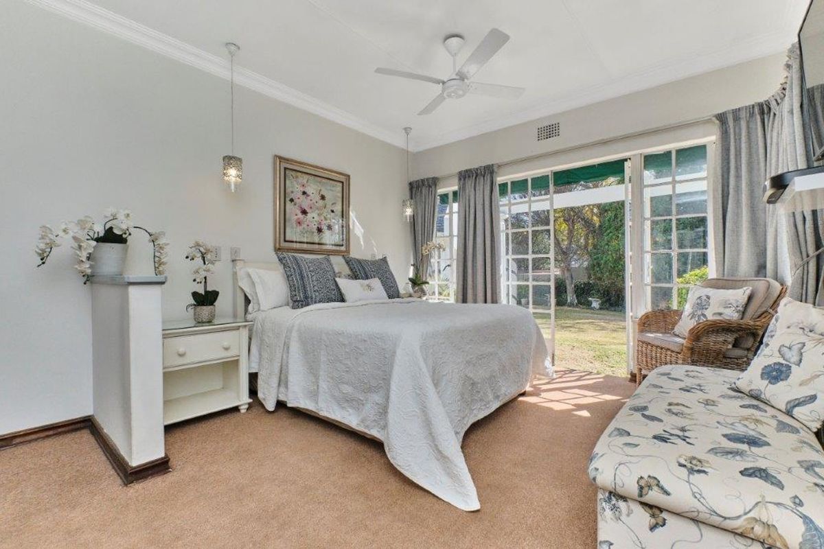 A bright bedroom featuring crown molding, a ceiling fan, and large glass french doors providing direct access to the garden.