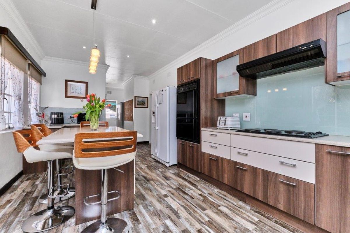 Modern kitchen featuring wood-grain cabinetry, stone countertops, integrated appliances, a gas hob with extractor, and a functional breakfast bar island.