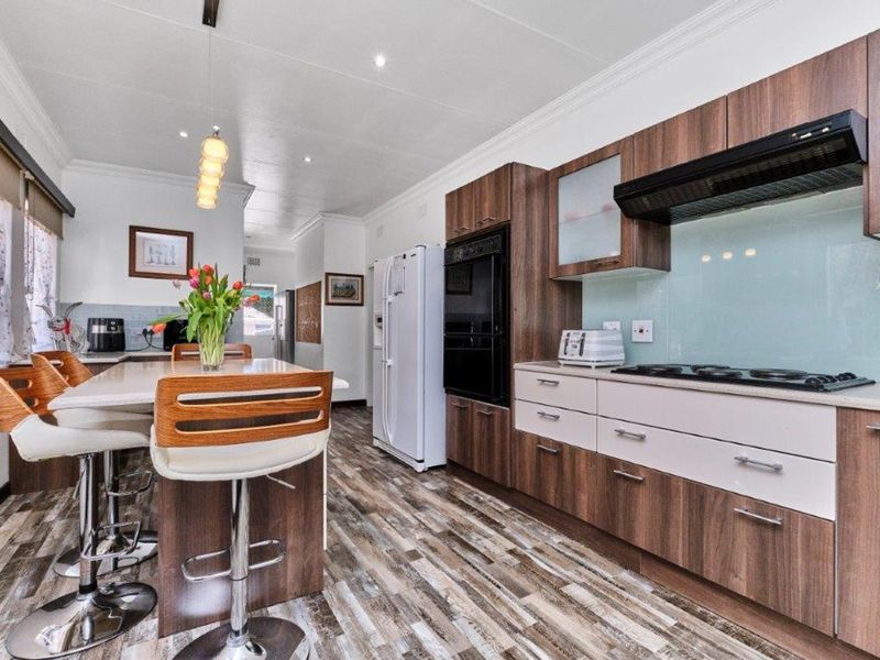 Modern kitchen featuring wood-grain cabinetry, stone countertops, integrated appliances, a gas hob with extractor, and a functional breakfast bar island.