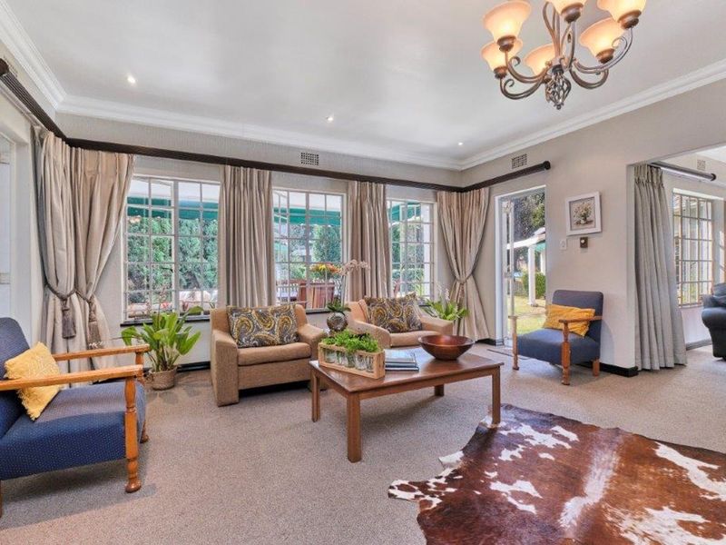 Spacious living room featuring crown molding, recessed lighting, a decorative chandelier, and large windows with direct access to the garden through french doors.