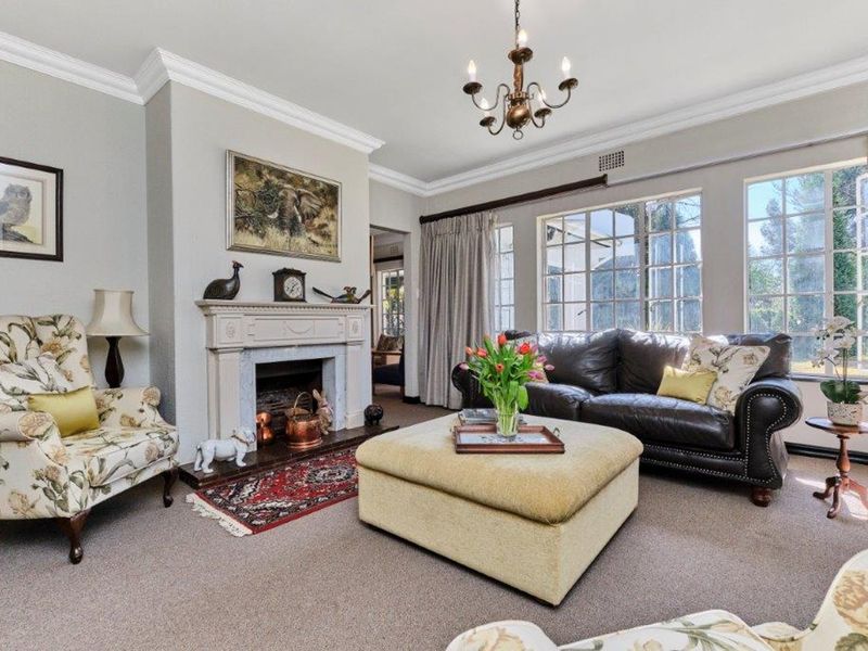 A well-maintained living room featuring a classic fireplace with a mantelpiece, crown molding, and large multi-pane windows that provide ample natural light.
