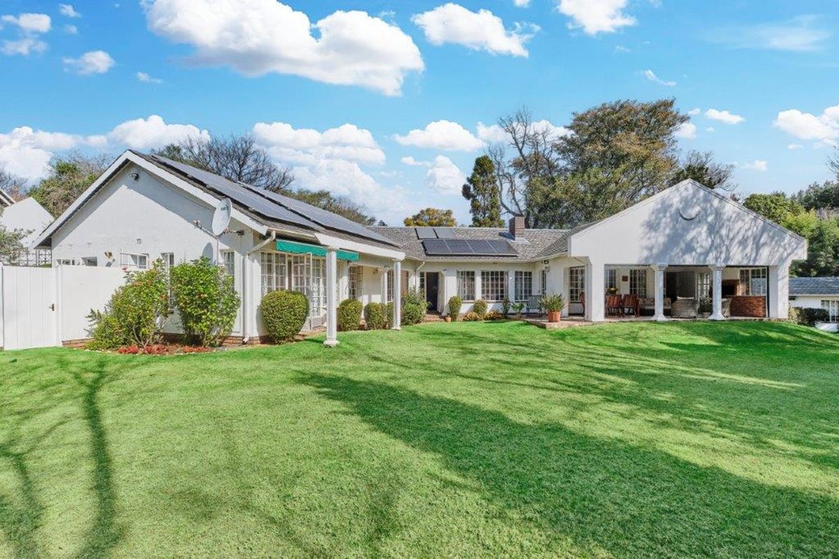Spacious rear garden view featuring a well-maintained lawn, covered patio area, and solar panels installed on the roof.