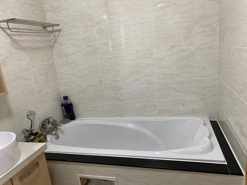 A functional bathroom featuring a built-in bathtub with tiled surround, vanity basin, and chrome fixtures. Requires minor maintenance to the bathtub access panel.