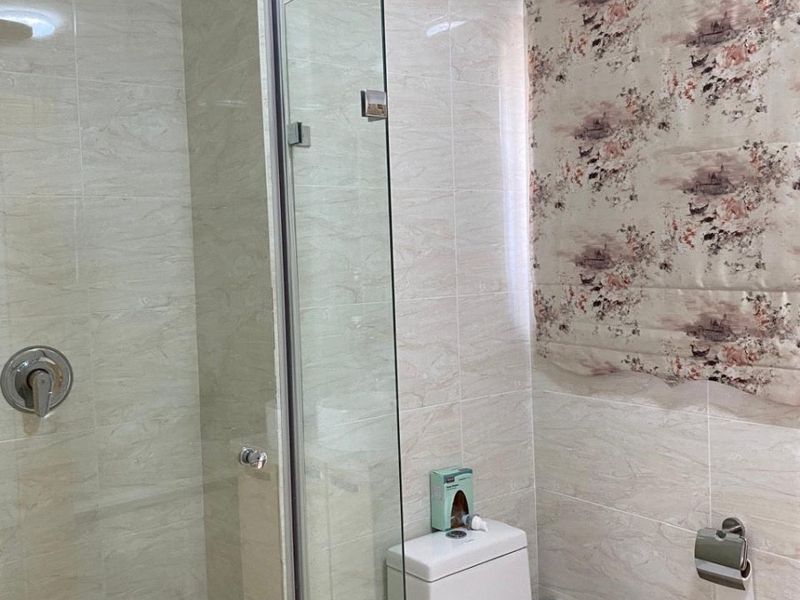 A modern bathroom featuring a glass-enclosed shower with a rainfall shower head, neutral wall tiling, and a contemporary toilet.