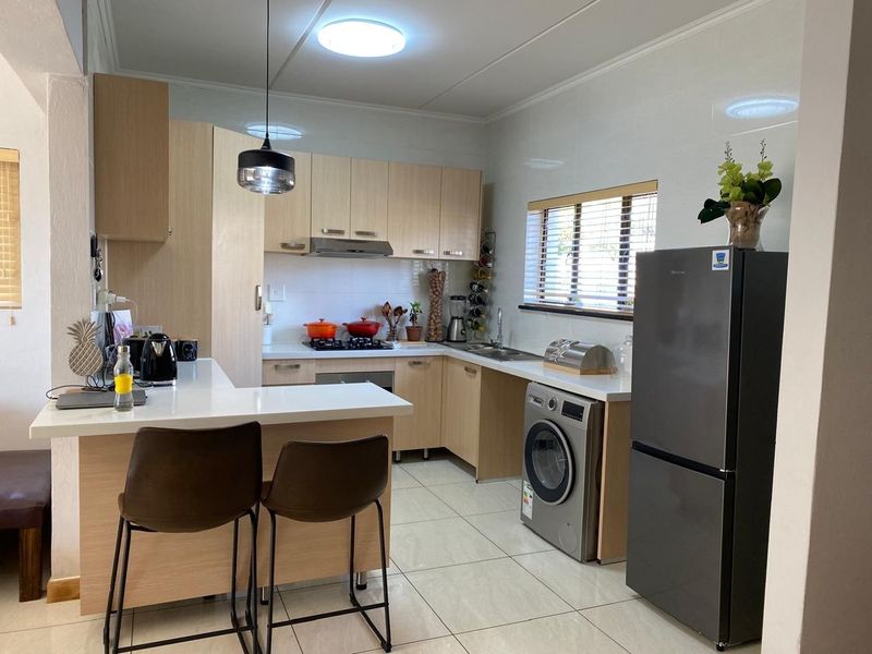 Modern kitchen featuring light wood cabinetry, stone countertops, a breakfast bar, and integrated appliances, finished with clean tiled flooring and contemporary lighting.