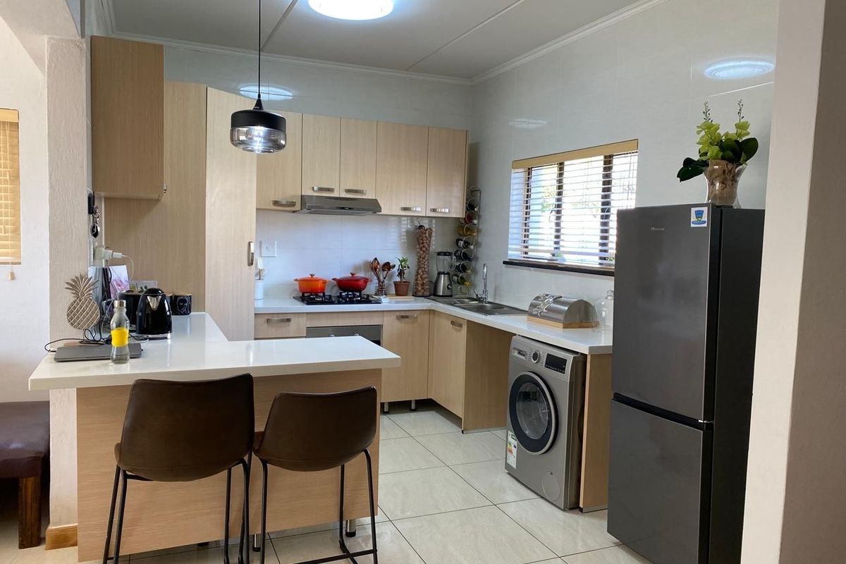 Modern kitchen featuring light wood cabinetry, stone countertops, a breakfast bar, and integrated appliances, finished with clean tiled flooring and contemporary lighting.