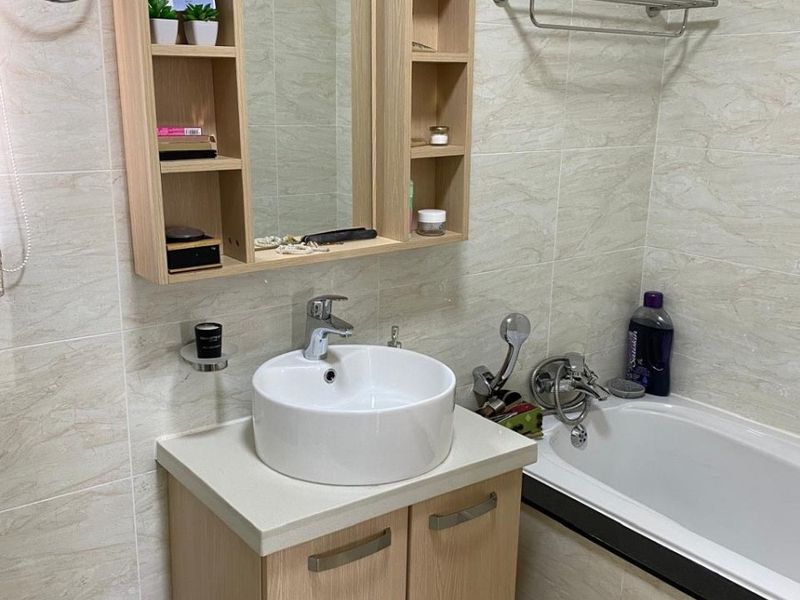 A functional bathroom featuring a vessel sink vanity, integrated wall shelving, and a bathtub with tiled wall finishes.