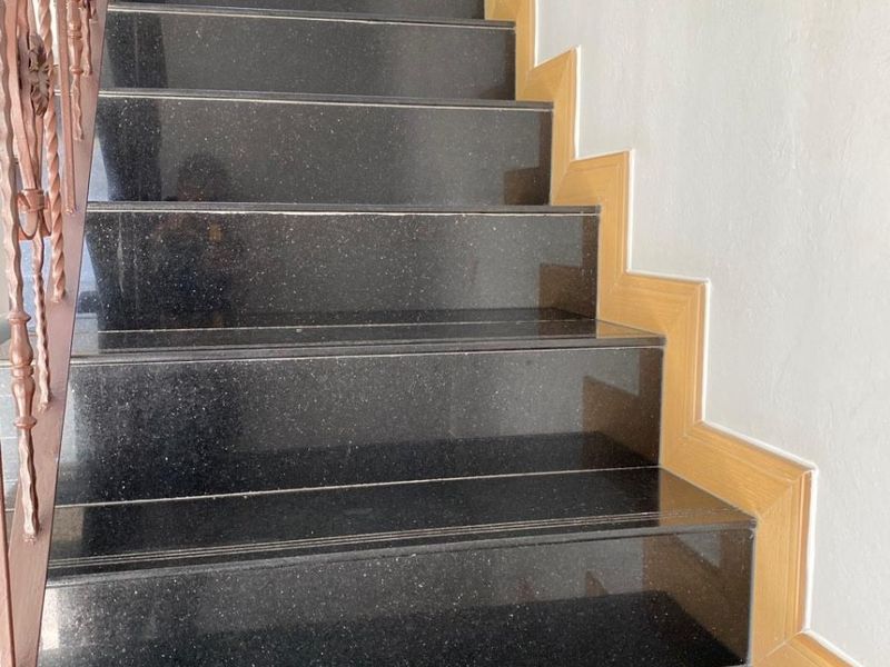 A staircase featuring polished black granite treads and risers, complemented by a decorative wrought iron balustrade and timber skirting.