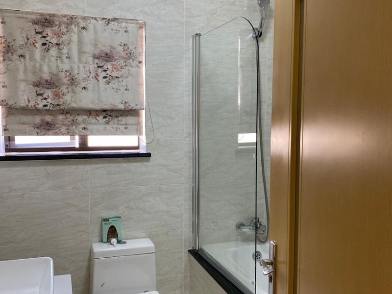 A functional bathroom featuring a bathtub with a glass shower screen, a modern toilet, and a vanity basin with tiled wall finishes.