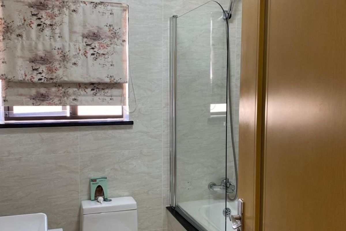 A functional bathroom featuring a bathtub with a glass shower screen, a modern toilet, and a vanity basin with tiled wall finishes.