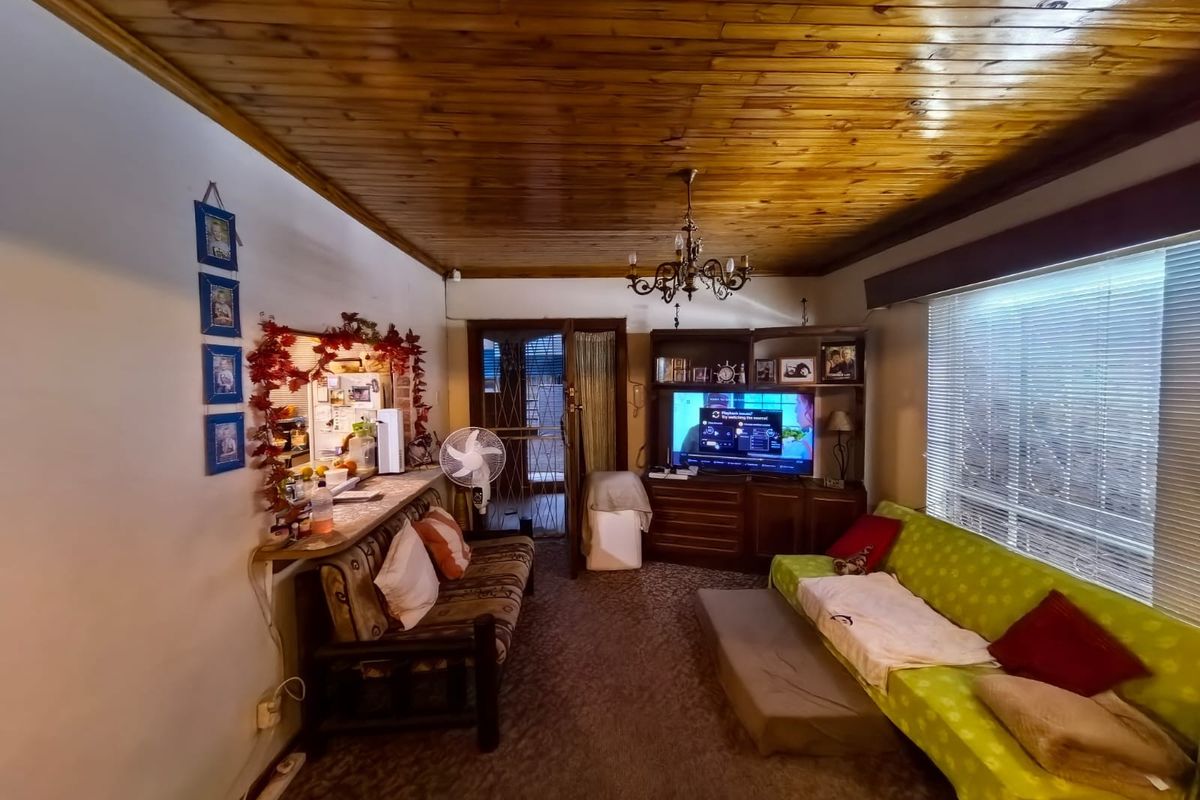 A living room featuring a timber tongue and groove ceiling, a central chandelier, and built-in shelving, offering a dated aesthetic ready for modernization.