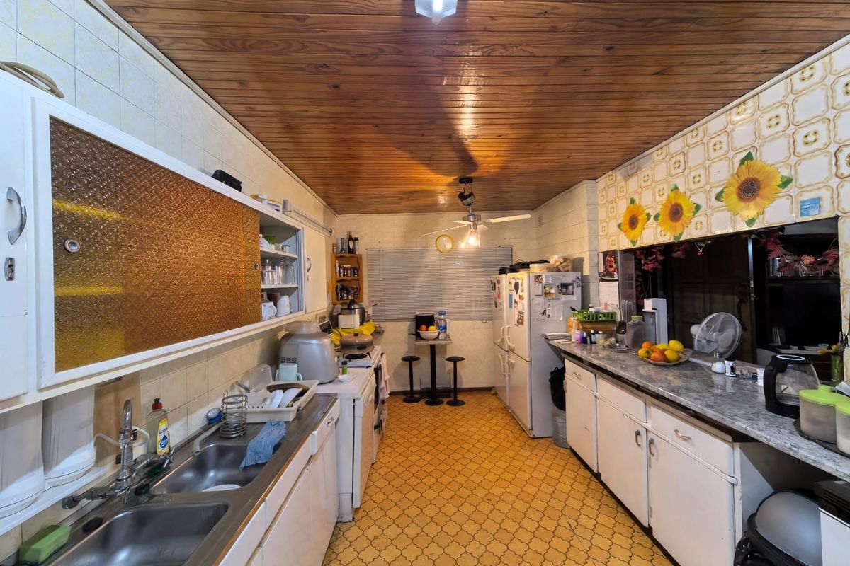 A functional kitchen featuring double stainless steel sinks, laminate countertops, built-in cabinetry, and a timber ceiling, offering significant potential for modern renovation.