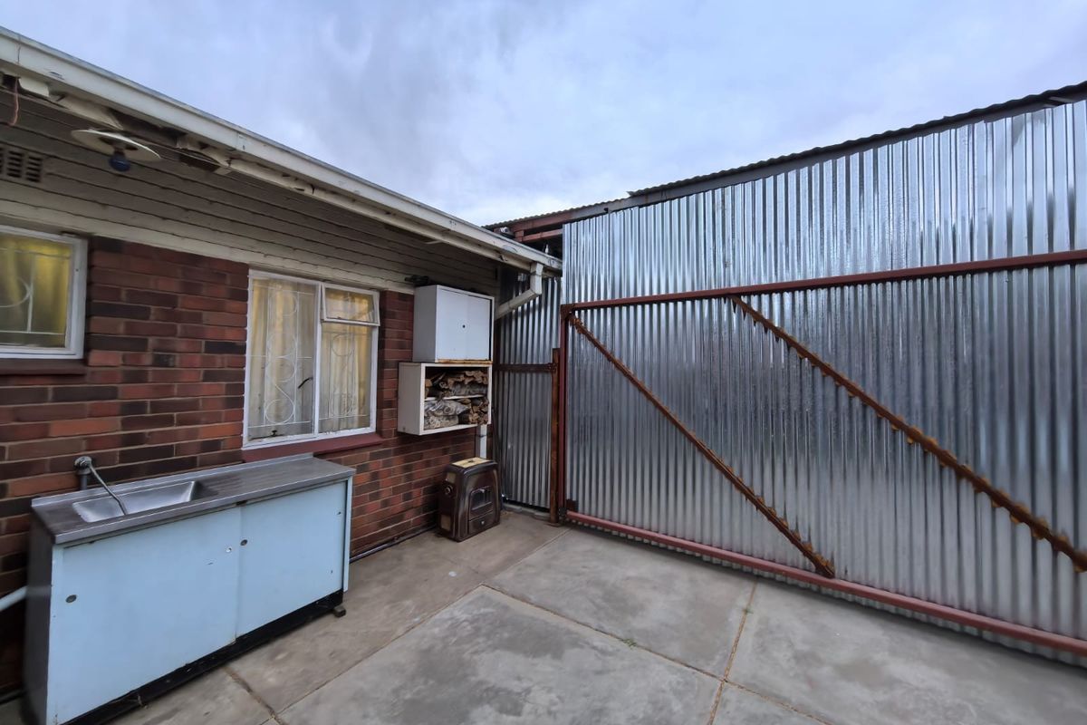 Rear exterior area featuring a brick facade, concrete paving, an external sink, and a large corrugated metal sliding gate.