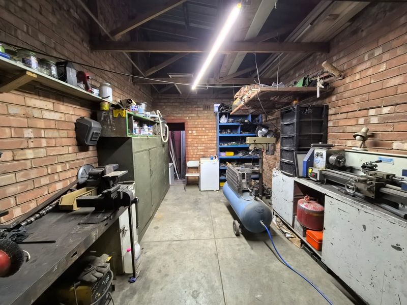 A functional workshop or garage space featuring exposed brick walls, concrete flooring, and exposed timber roof trusses, suitable for industrial or hobby use.