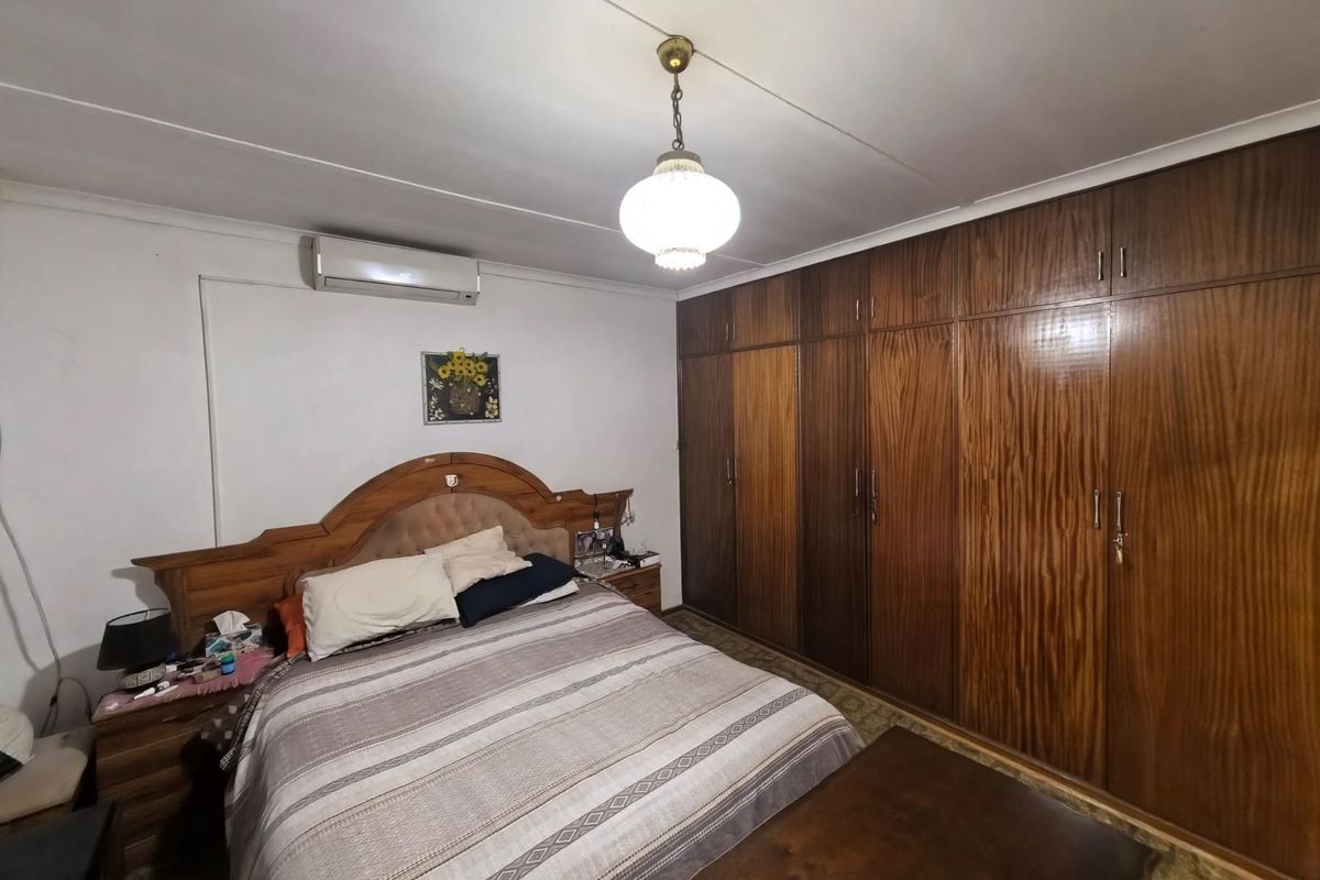 A bedroom featuring extensive built-in wooden cabinetry, a wall-mounted air conditioning unit, and a central pendant light fixture.