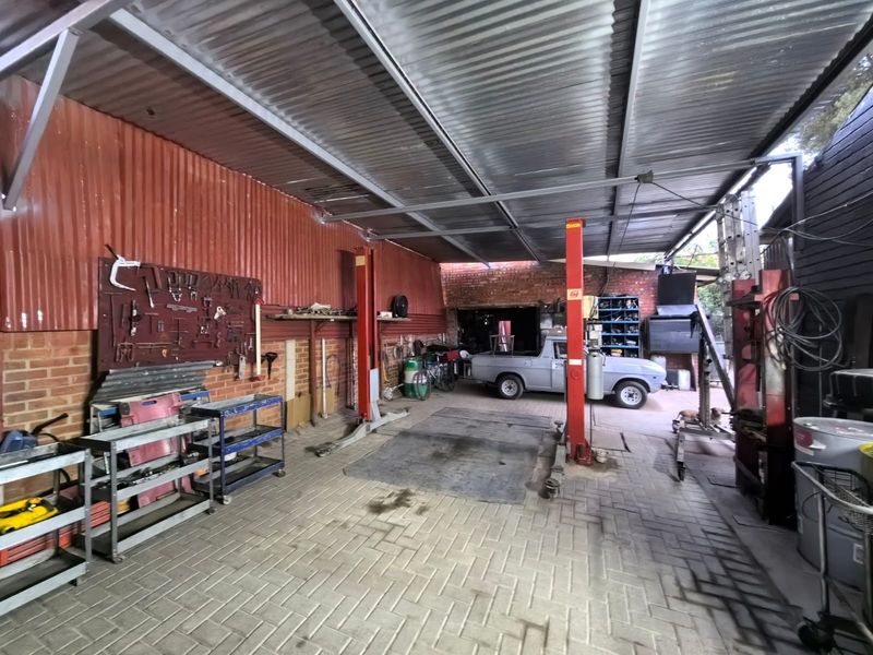 A functional commercial workshop or garage space featuring a two-post vehicle lift, durable paved flooring, and corrugated metal roofing.