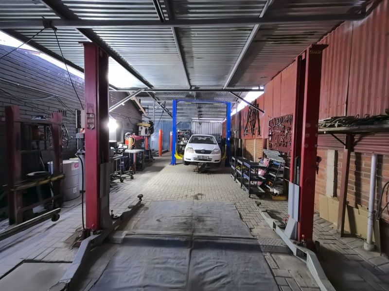 Commercial garage workshop featuring a two-post vehicle lift, corrugated metal roofing, and paved flooring, suitable for automotive repair operations.