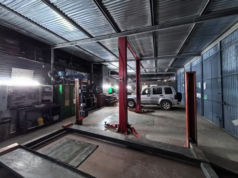 A functional commercial garage space featuring a two-post vehicle lift, high corrugated metal ceilings, and durable concrete flooring, suitable for automotive repair operations.
