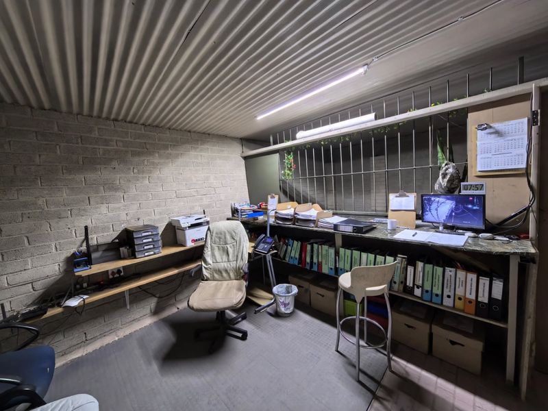 A functional office space featuring exposed brick walls, a corrugated metal ceiling, and built-in desk cabinetry with integrated security bars.