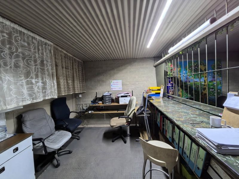 A functional office space featuring exposed brick walls, a corrugated metal ceiling, and a built-in service counter with security bars.