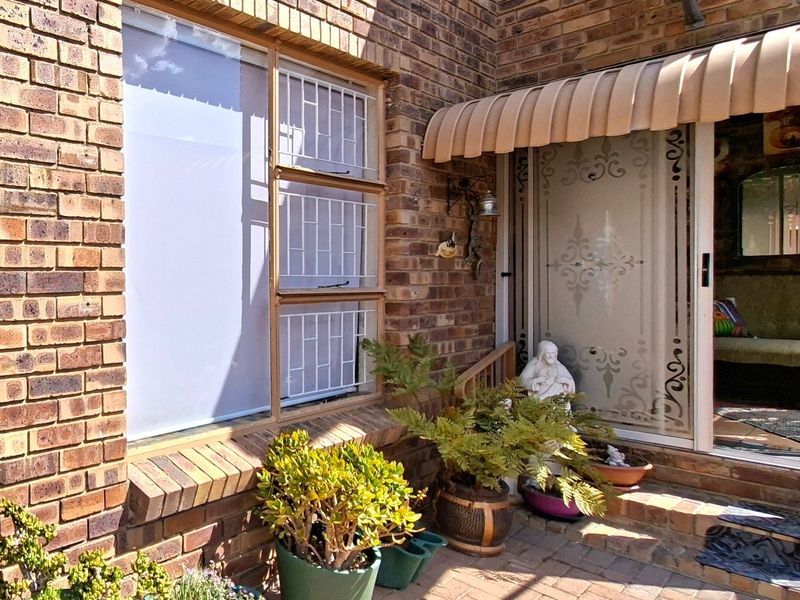 A paved patio area featuring a brick facade, protective security bars on the window, and a retractable awning over the sliding glass entrance.