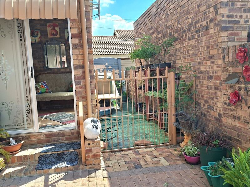 Rear exterior view of a townhouse featuring brick paving, a metal security gate, and a sliding glass door with a retractable awning.