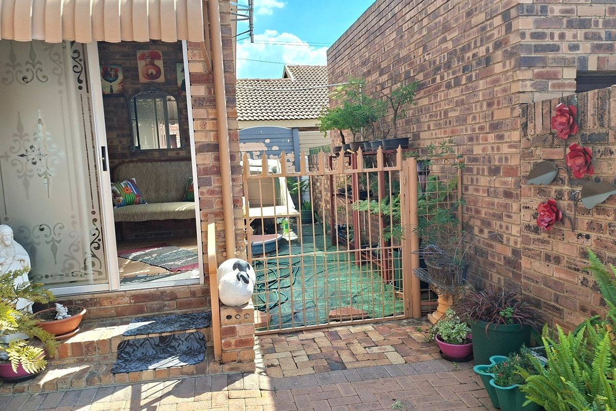 Rear exterior view of a townhouse featuring brick paving, a metal security gate, and a sliding glass door with a retractable awning.