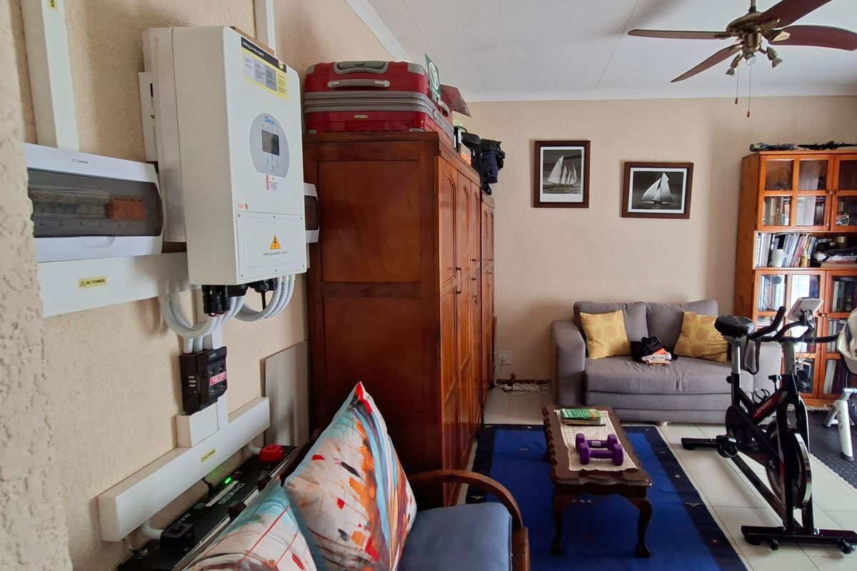 A living room area featuring a ceiling fan, tiled flooring, and a wall-mounted inverter system with an electrical distribution board.